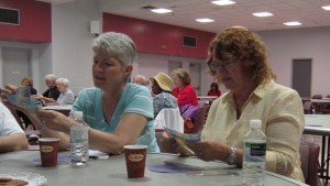 A table with several seniors looks closely at paper bills given to them to inspect.  They were asked to decide if the money was counterfeit – none of it was.