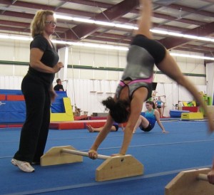 The first part of this gymnastic routine is to mount the small bar.  The athlete has to run towards the small bar on the floor, reach down with her hands and grasp the bar and then swing her body into an upright position and hold her body steady as she prepares to move into the twirl part of the routine.  Here Kathy Kline, the athlete who runs the program prepares to steady an athlete.