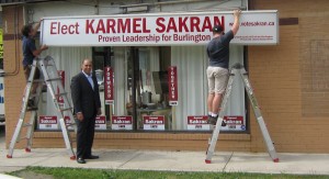 Liberal candidate Karmel Sakran stands proudly before the sign being installed outside his campaign office on Guelph Line