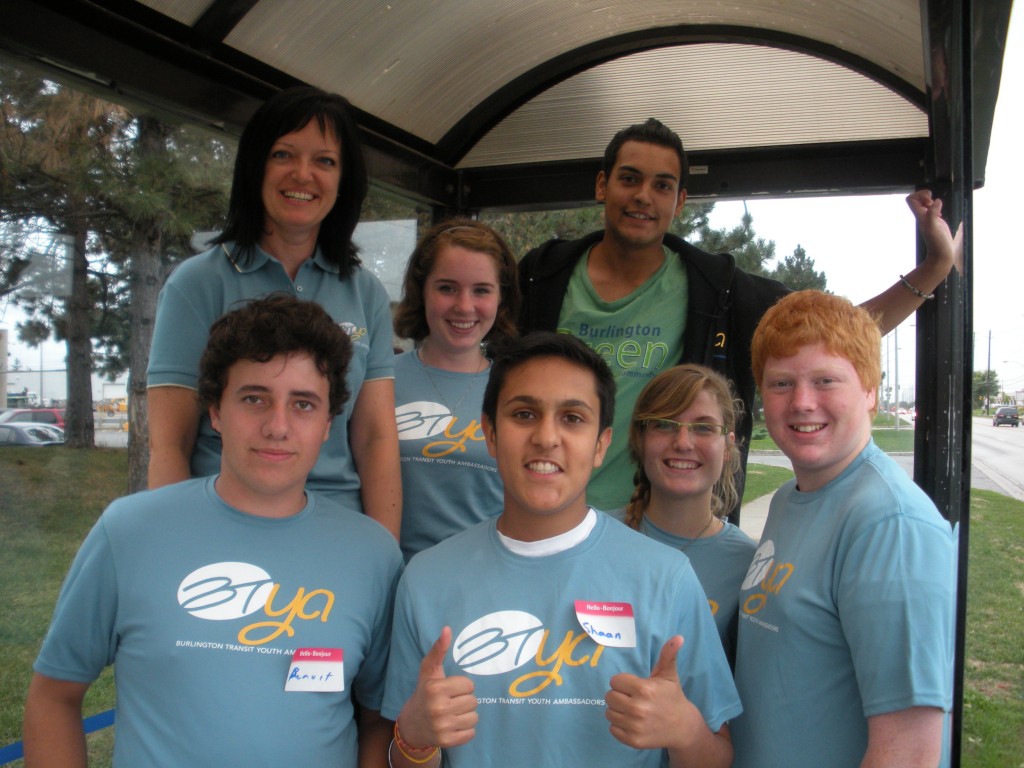 Burlington Transit Youth Ambassadors gather in a bus shelter. Front row: YAs Benoit, Shaan, Billi and Harrison. Back row, BT’s Sandra Maxwell, YA Kayla and Burlington Green advisor Kale.