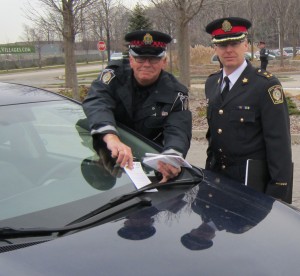 Auxiliary police officer Voorberg tucks a notice under a car windshield as Deputy Chief Andrew Fletcher makes sure it gets done right.  Both were taking part in the Lock it or Lose it Campaign that was launched at Tansley Wood Friday morning.