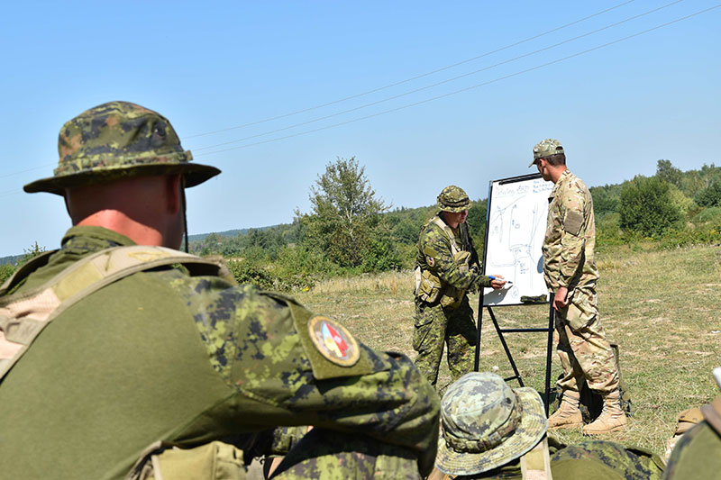 A Canadian soldier explains the conduct of a patrolling raid to a Ukrainian platoon during small team training at the International Peacekeeping and Security Centre in Starychi, Ukraine, on September 1, 2016. Photo : JTF-U AK51-2016-069-03 ~ Photo : JTF-U AK51-2016-069-03